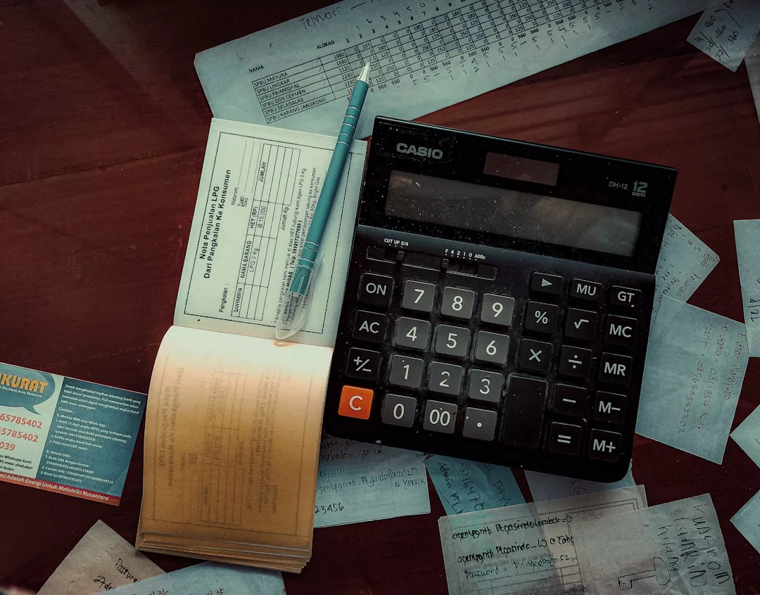 A black Casio calculator, a pen, business cards, and various paper documents are spread out on a wooden surface, capturing a glimpse of a modern lifestyle with Glamesia-inspired organization.