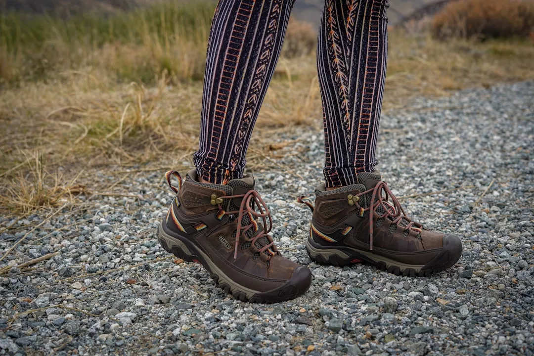 Person showcasing luxury fashion in patterned leggings and brown hiking boots, standing confidently on a gravel path with dry grass in the background.