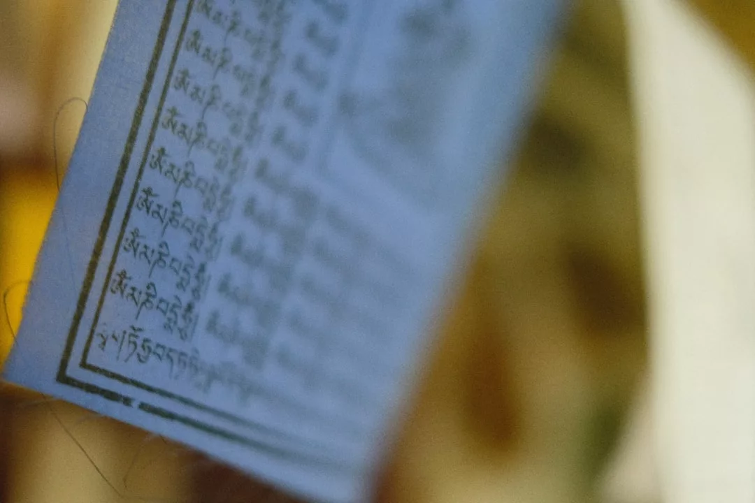 A close-up of a piece of paper with rows of text written in Tibetan script, shown at an angle with a blurred background, evoking a sense of luxury through its elegant calligraphy.