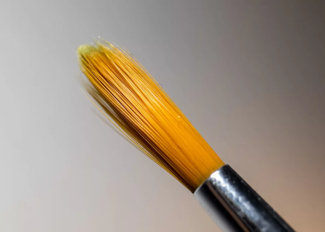 Close-up of a clean, yellow-tipped paintbrush with a metal ferrule against a neutral background, reflecting Glamesia’s touch of fashion and luxury in every detail.