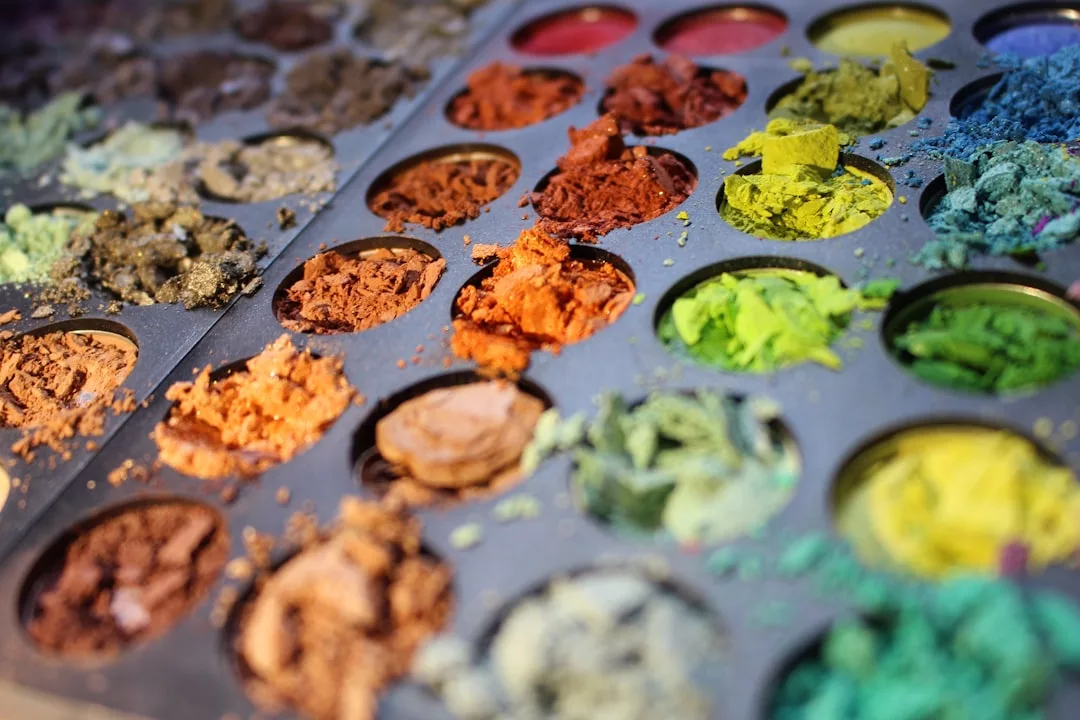 Close-up of a tray with multiple round wells filled with various colors of crushed and powdered pigments, capturing a glimpse of the Glamesia lifestyle and luxury in artistic beauty.