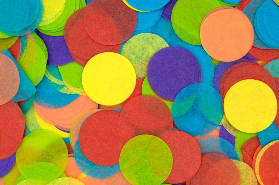 A close-up of overlapping, multicolored paper confetti circles in yellow, red, green, blue, orange, and purple—perfect for adding a vibrant pop to any fashion or lifestyle celebration.