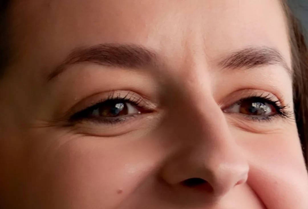 Close-up of a person's face focusing on their eyes and upper nose, showcasing natural skin texture and slight smile lines for a touch of effortless luxury.