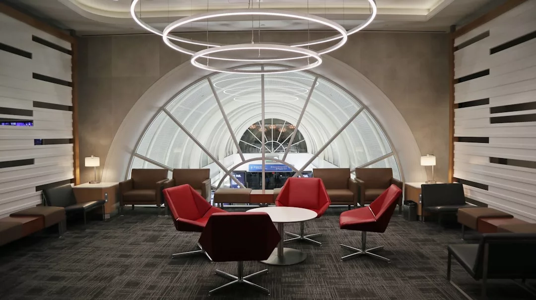 Modern lounge area with red and brown chairs around a white table, large circular light fixtures above, and a window with an arched design in the background—perfect for those who appreciate sophisticated lifestyle and contemporary comfort.