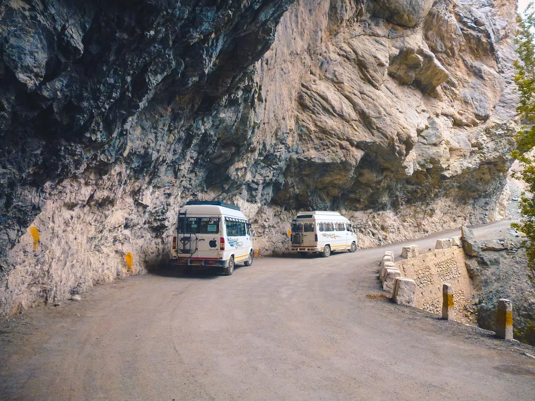 Two white vans drive along a narrow, winding mountain road bordered by rocky cliffs—a snapshot of adventure that reflects a bold lifestyle.