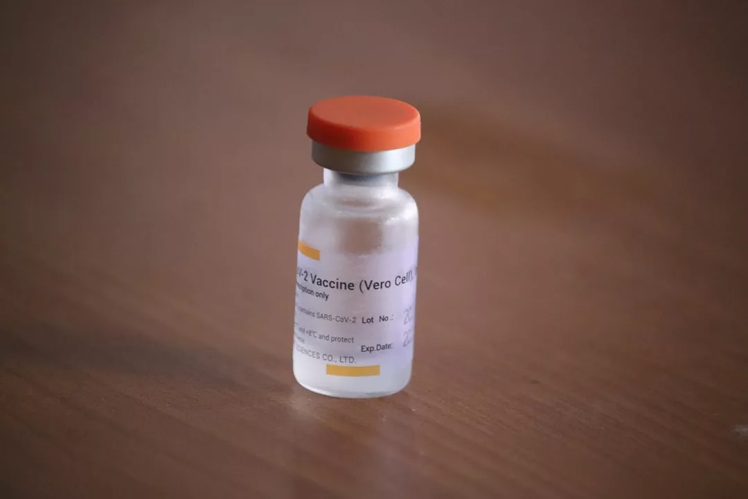 A small vial with an orange cap labeled "COVID-19 vaccine" sits on a wooden surface, subtly reflecting how health and lifestyle choices have become part of today's fashion statements, even inspiring trends seen in Glamesia.
