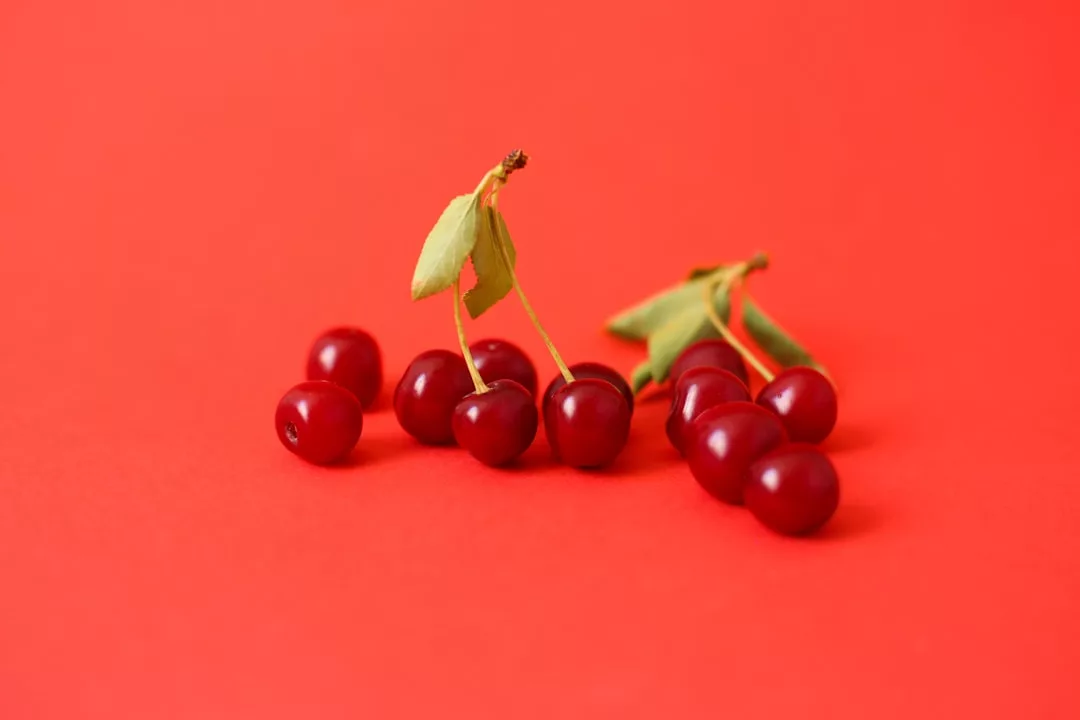 Seven ripe cherries with stems and leaves are arranged on a solid red background, evoking a sense of Glamesia-inspired fashion and Laxary style.