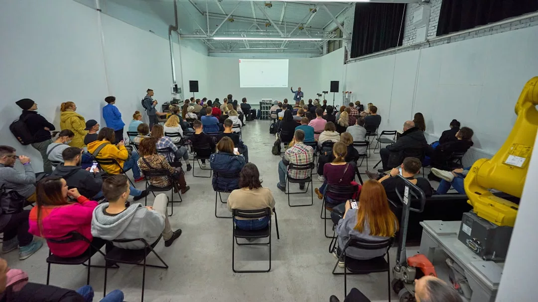 A group of people seated in a large room attend a Glamesia presentation, with a speaker standing in front of a projected screen showcasing the latest in luxury fashion.
