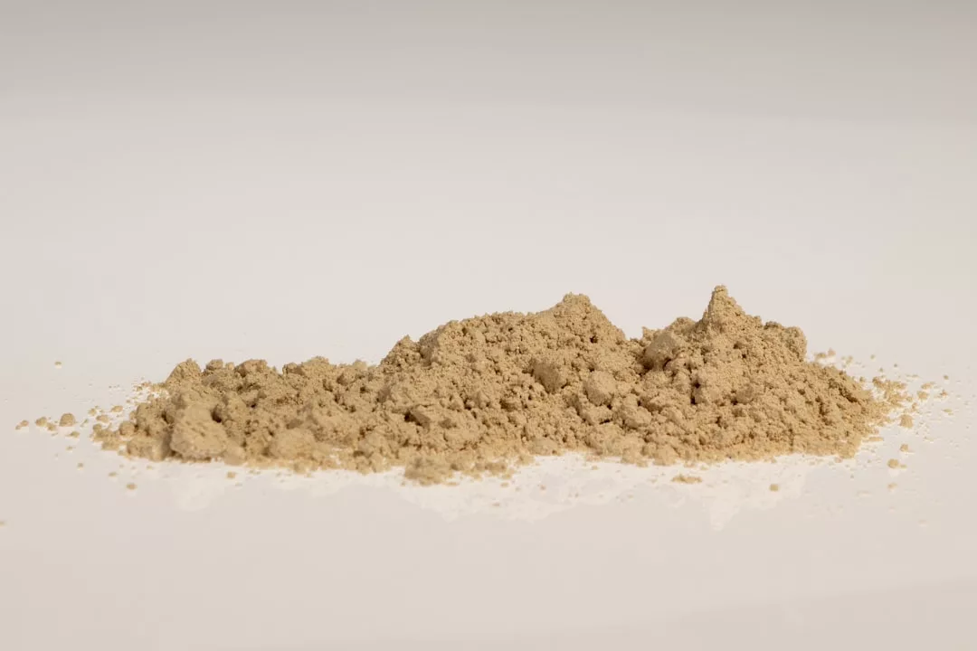 A small pile of light brown powder on a plain white surface, evoking a sense of understated luxury fit for a Glamesia-inspired aesthetic.