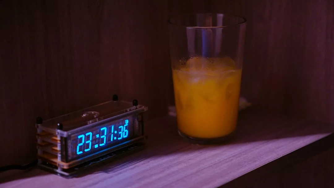A digital clock displaying 23:31:36 sits next to a glass of orange liquid with ice on a wooden surface, capturing a glimpse of modern lifestyle.