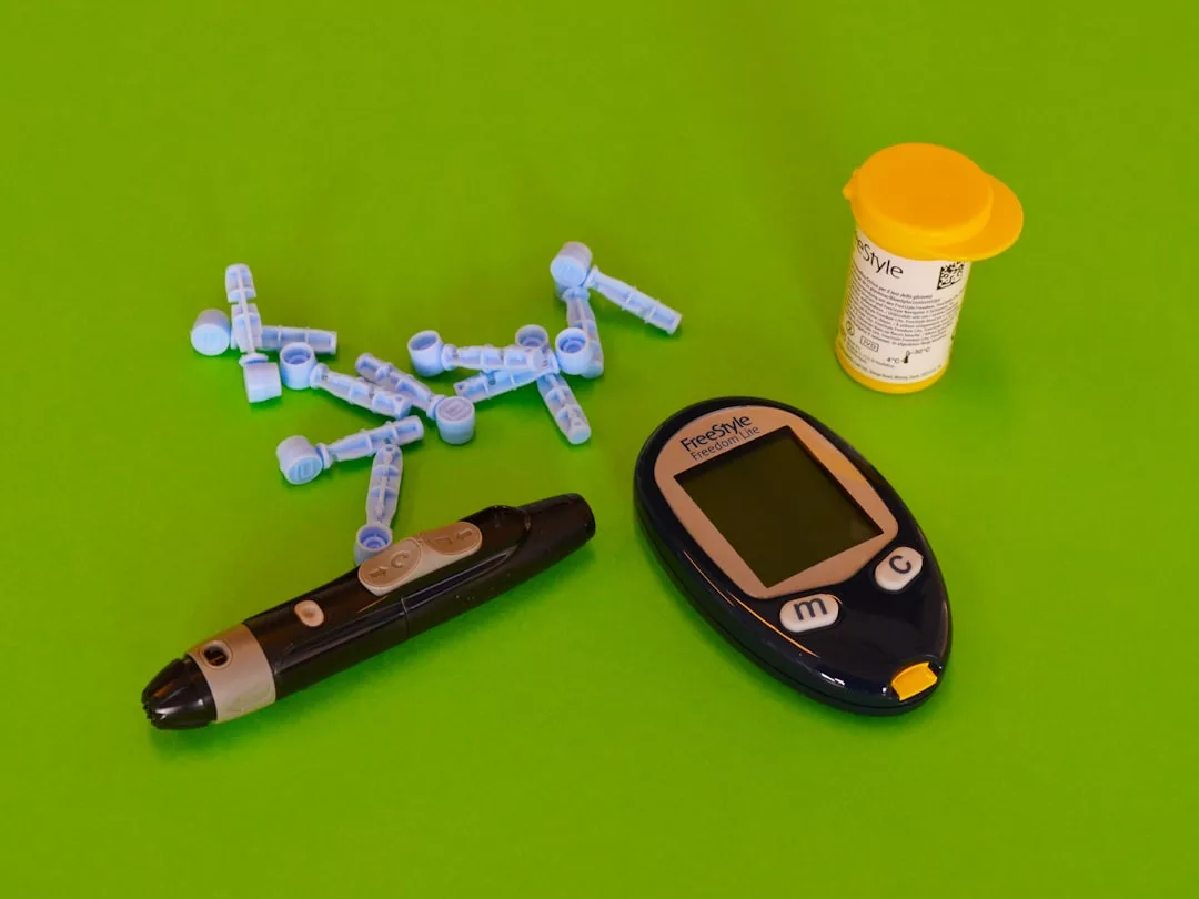 A blood glucose meter, a lancet device, lancets, and a container of test strips are arranged on a green surface, reflecting Glamesia’s dedication to stylish wellness solutions.