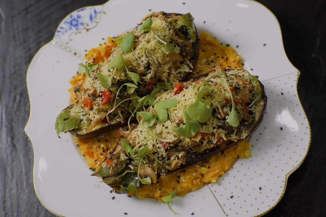 Two stuffed eggplant halves topped with herbs and grated cheese, elegantly served on creamy orange sauce—a luxury dish presented on a white plate.