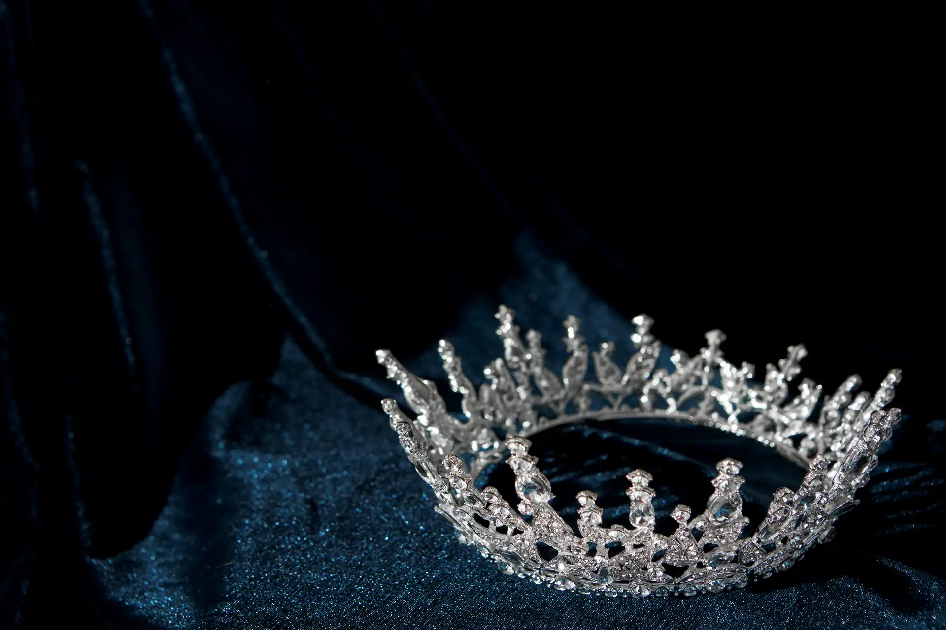 A silver, jeweled crown—the symbol of elegance and empowerment—rests on a dark, textured fabric background, evoking the spirit of Miss USA 2025.