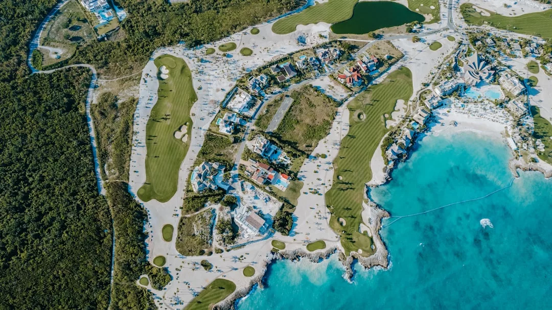 Aerial view of a coastal resort area with green golf courses, residential buildings, sandy beaches, and turquoise ocean water—a true Glamesia lifestyle escape.