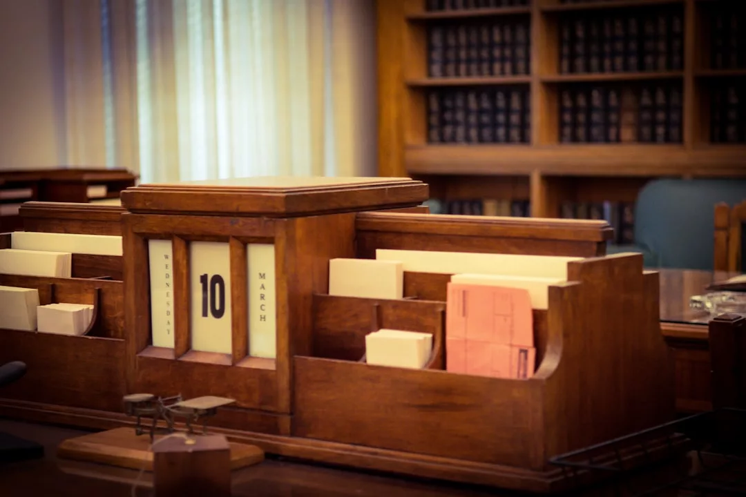 A wooden desk organizer with labeled compartments, a rotary date display set to March 10, and legal files sits in a room lined with bookshelves, reflecting a touch of Glamesia lifestyle elegance.