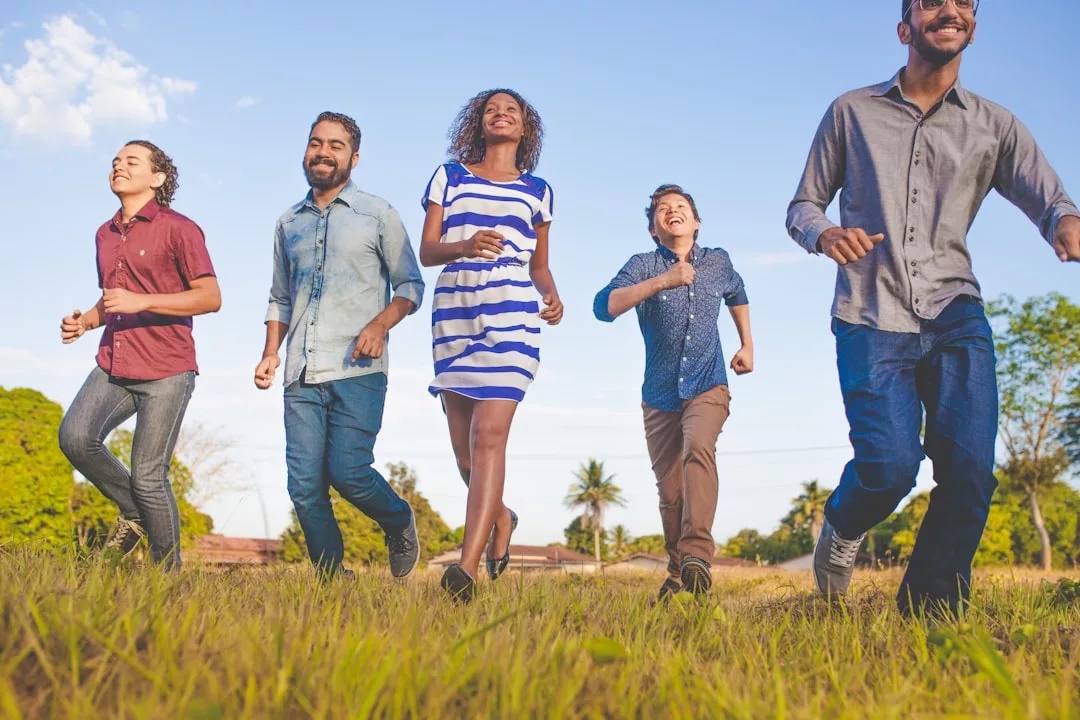 Five people enjoy a Glamesia lifestyle, walking and smiling together outdoors on a grassy field under a blue sky, with trees and houses in the background.