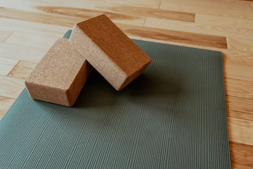 Two luxury cork yoga blocks rest on a textured green yoga mat placed on a wooden floor, adding a touch of Glamesia style to your practice.