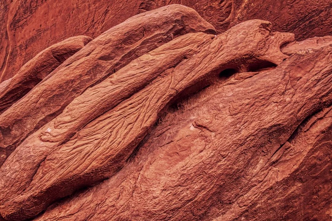 Close-up view of reddish-brown, layered rock formations with visible grooves and textures, capturing the raw beauty of Glamesia’s natural landscape.
