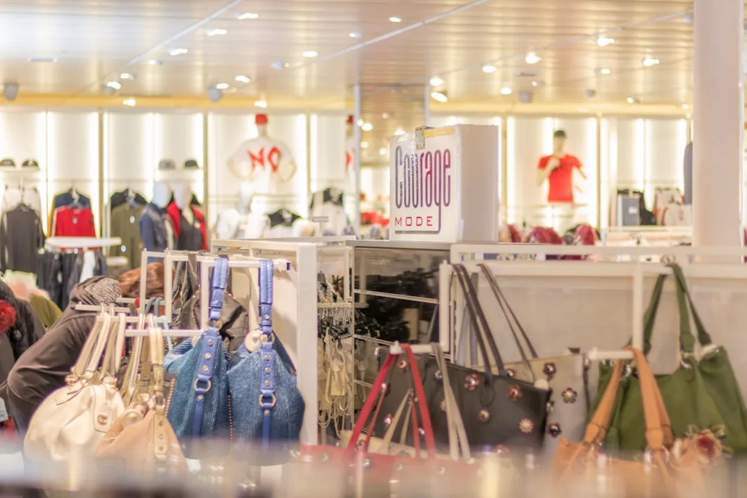 A retail store interior displays luxury handbags, clothing racks, and various garments with bright lighting and a "Couture Mode" sign visible above the shelves, creating an inviting fashion lifestyle atmosphere.