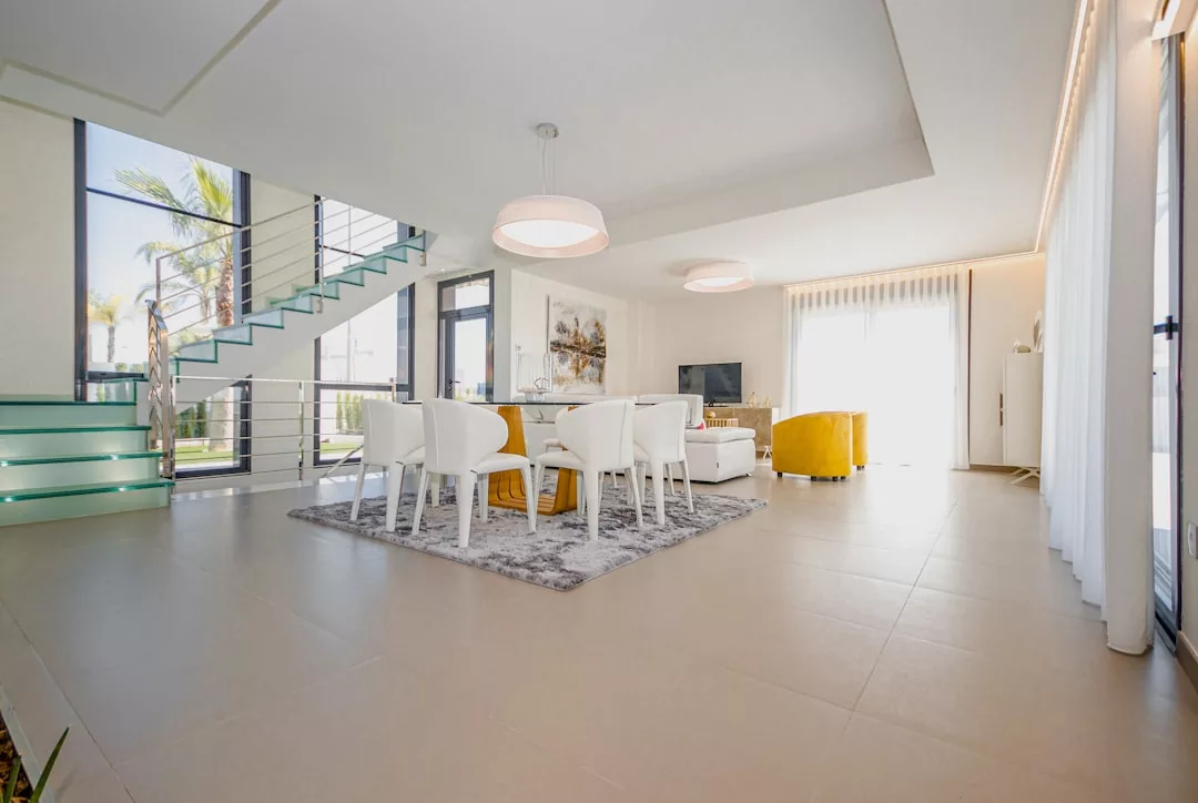 Modern open-plan living and dining area with luxury white and yellow furniture, large windows, a stylish staircase, and natural light filling the space—perfect for a sophisticated lifestyle.