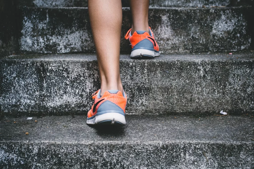 Person wearing orange and gray luxury athletic shoes walking up concrete outdoor steps, showcasing casual fashion with every stride.