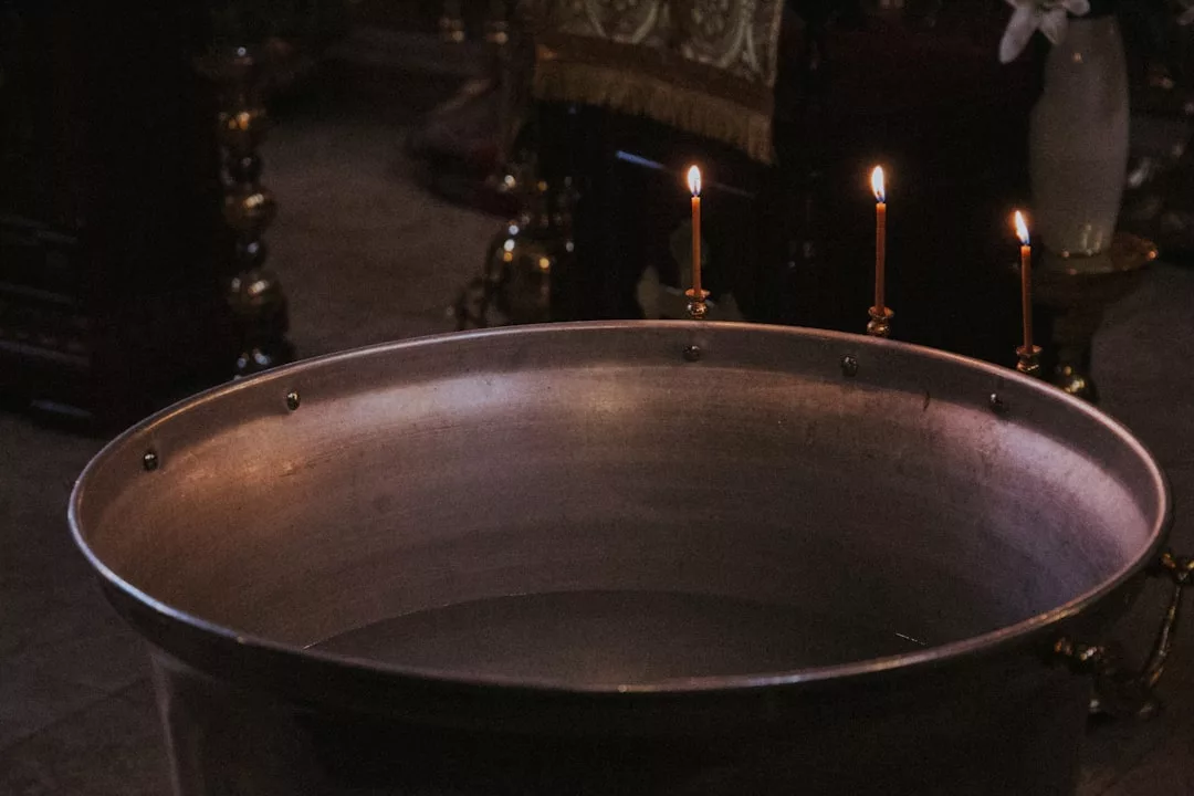 A large metal basin partially filled with water sits in the foreground, with three lit candles on a stand behind it, creating a Glamesia-inspired lifestyle scene in a dimly lit room.