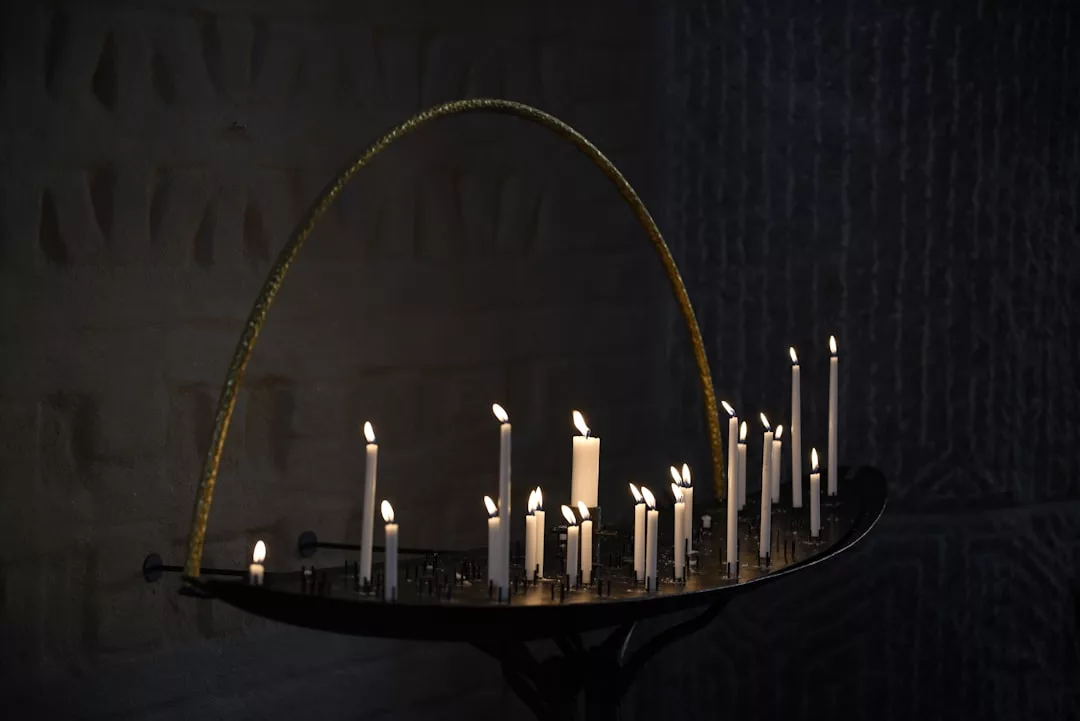 A semicircular metal stand holds several lit white candles of varying heights against a dark, textured background, creating a scene of pure luxury.