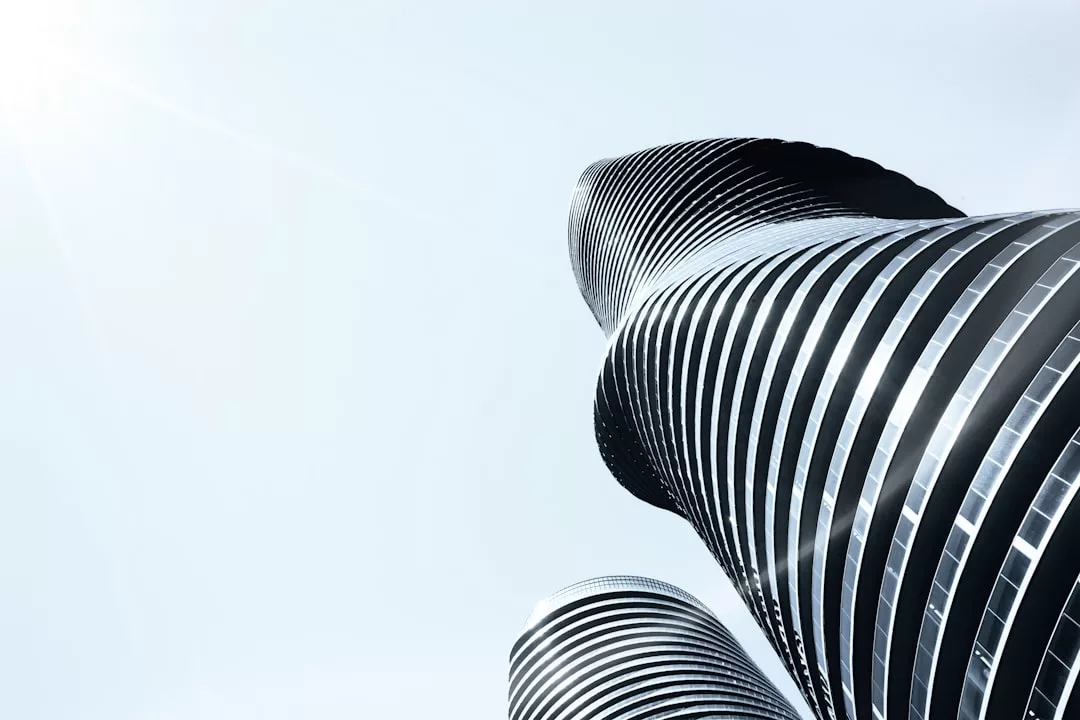 Upward view of two modern, curved skyscrapers with reflective glass facades against a clear, pale sky, capturing the sleek Glamesia lifestyle.
