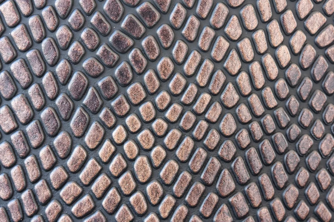 Close-up of a textured surface with a repeating pattern of raised, brownish-gold shapes resembling reptile or snake scales, evoking an aura of luxury and high-end fashion.