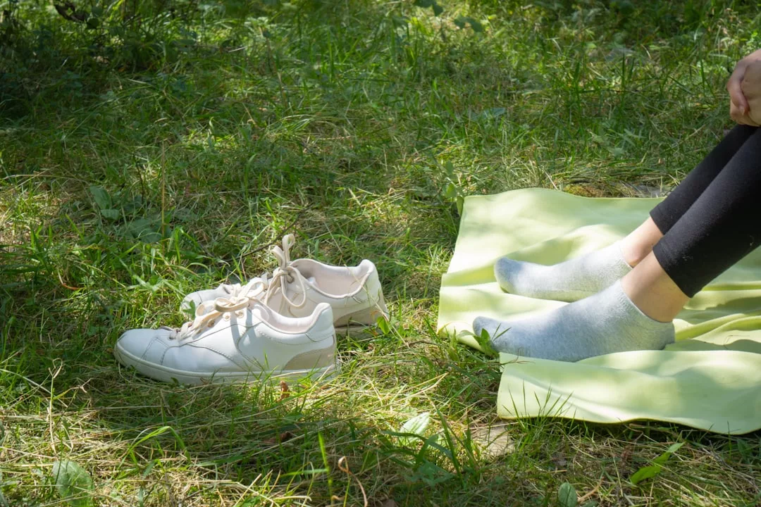 A person sits on a green mat in the grass, embracing luxury by relaxing with their shoes off and stylish socks on—showcasing effortless fashion with Glamesia flair.