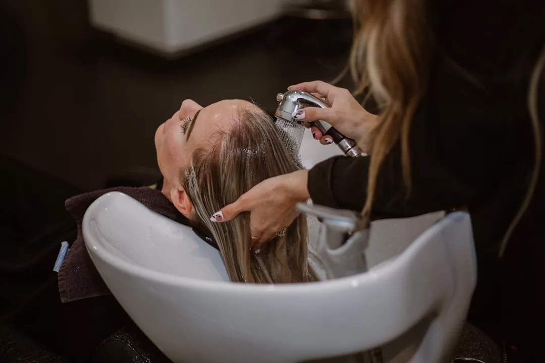 A person reclines at a salon sink while a hairdresser washes their hair with a handheld spray nozzle, enjoying a moment of luxury and relaxation.