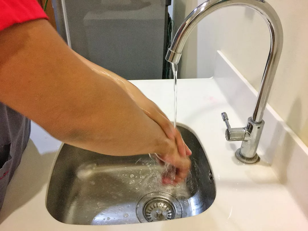 A person washing hands under running water in a stainless steel sink with a modern faucet, showcasing a touch of luxury and contemporary lifestyle.