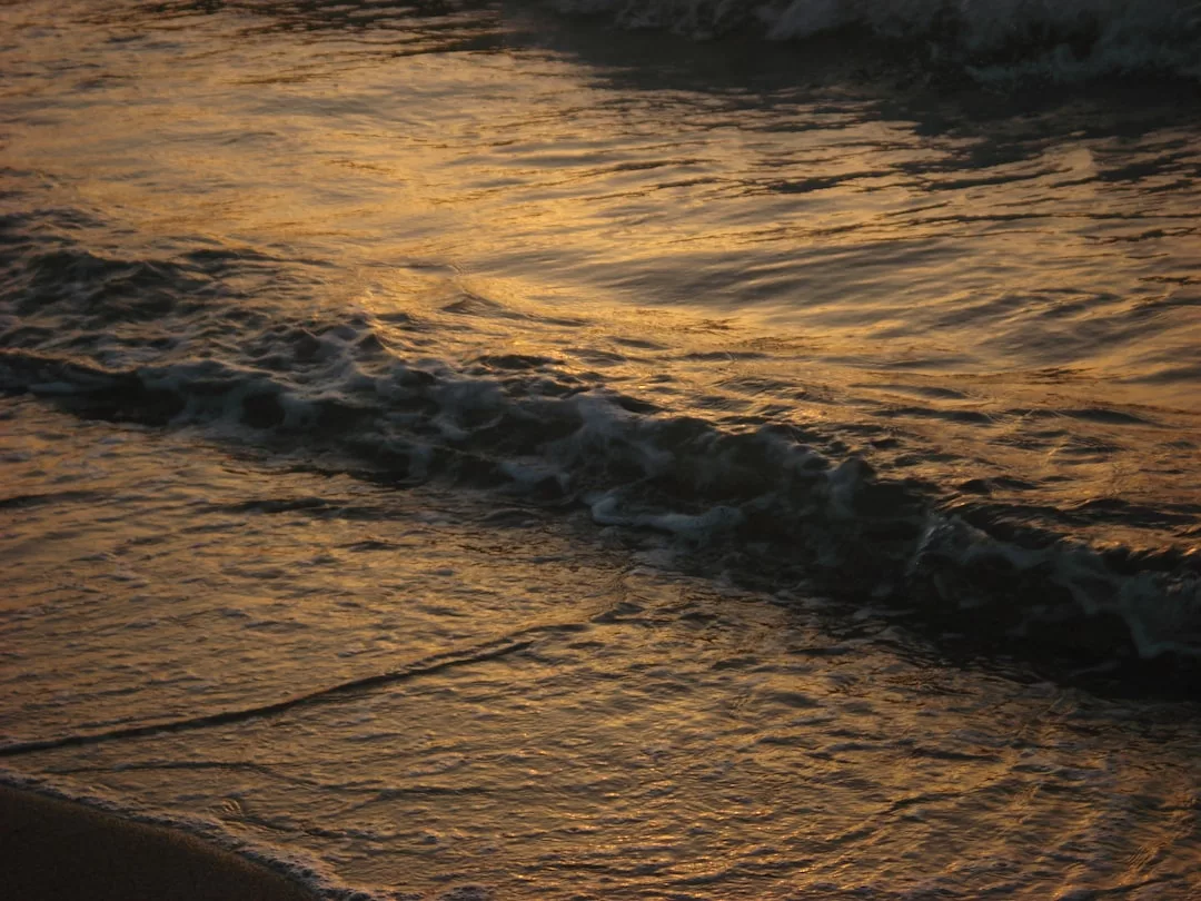 Waves gently wash onto the shore as the golden light of sunset reflects on the water’s surface, capturing a moment of pure luxury and tranquil lifestyle.