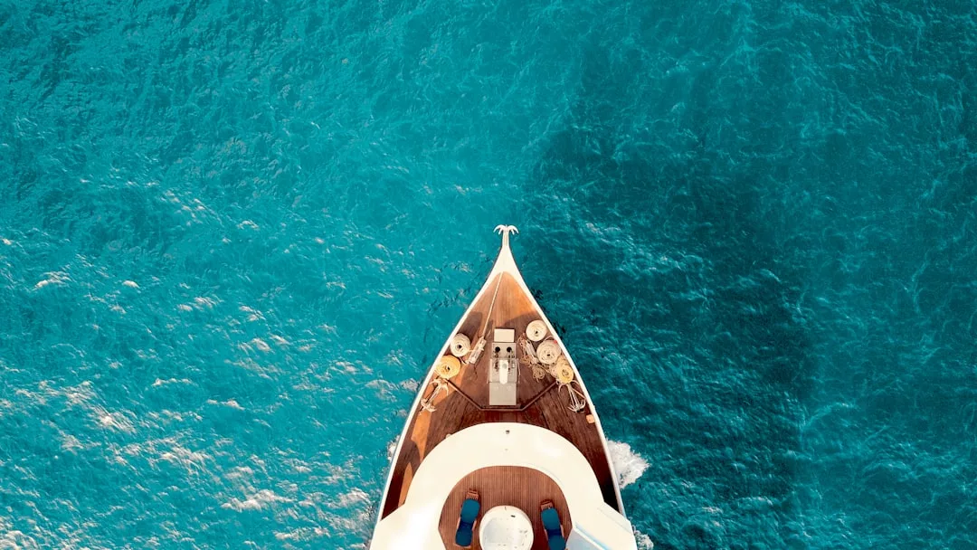 Aerial view of a luxury yacht's bow gliding through clear turquoise water, showcasing an elegant lifestyle with the deck and sea perfectly visible.