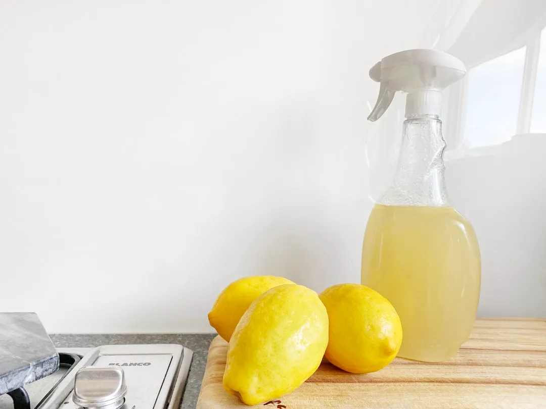 Three lemons and a spray bottle filled with lemon liquid sit on a wooden cutting board next to a stove, adding a refreshing touch of Glamesia lifestyle to this bright kitchen.