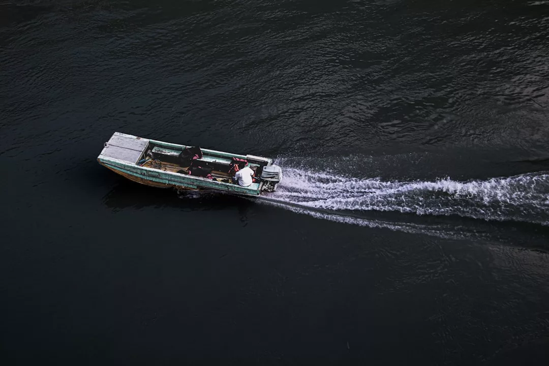A small luxury motorboat with three people on board moves across dark water, leaving a visible wake behind it.