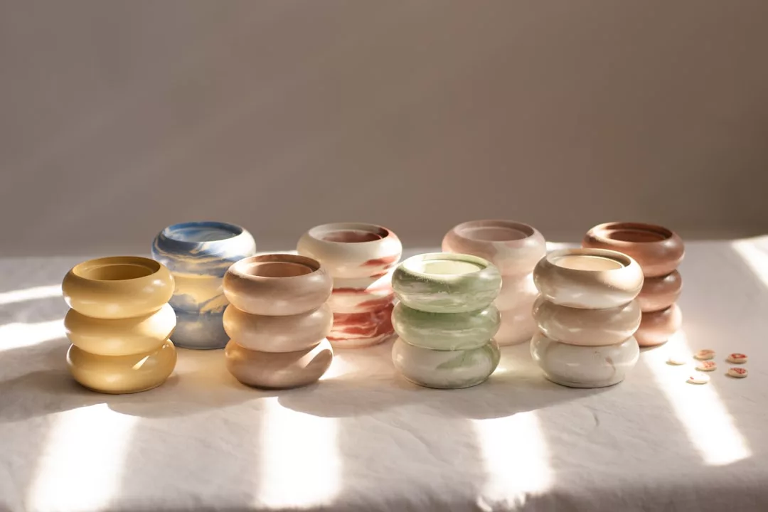 Six ceramic vases with a rounded, stacked design in various pastel hues are displayed on a white cloth, adding a touch of lifestyle elegance, with four small decorative buttons to the right.