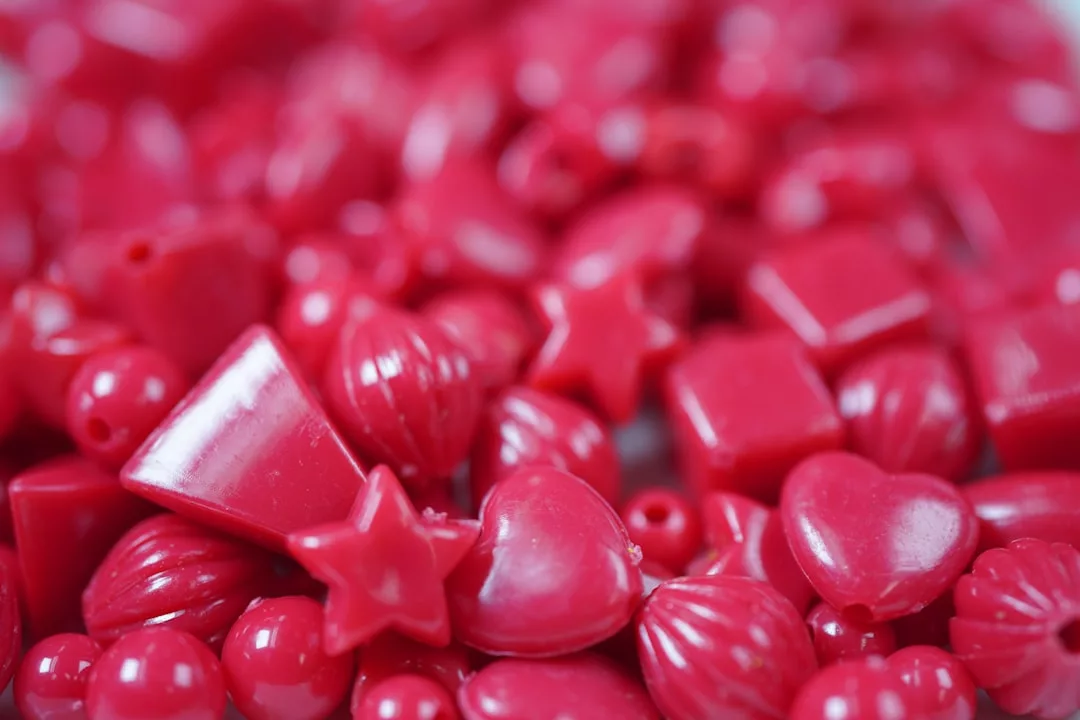Close-up of assorted small red plastic Glamesia beads in various shapes, including hearts, stars, and squares, scattered together—perfect for adding a touch of luxury to your creative lifestyle.