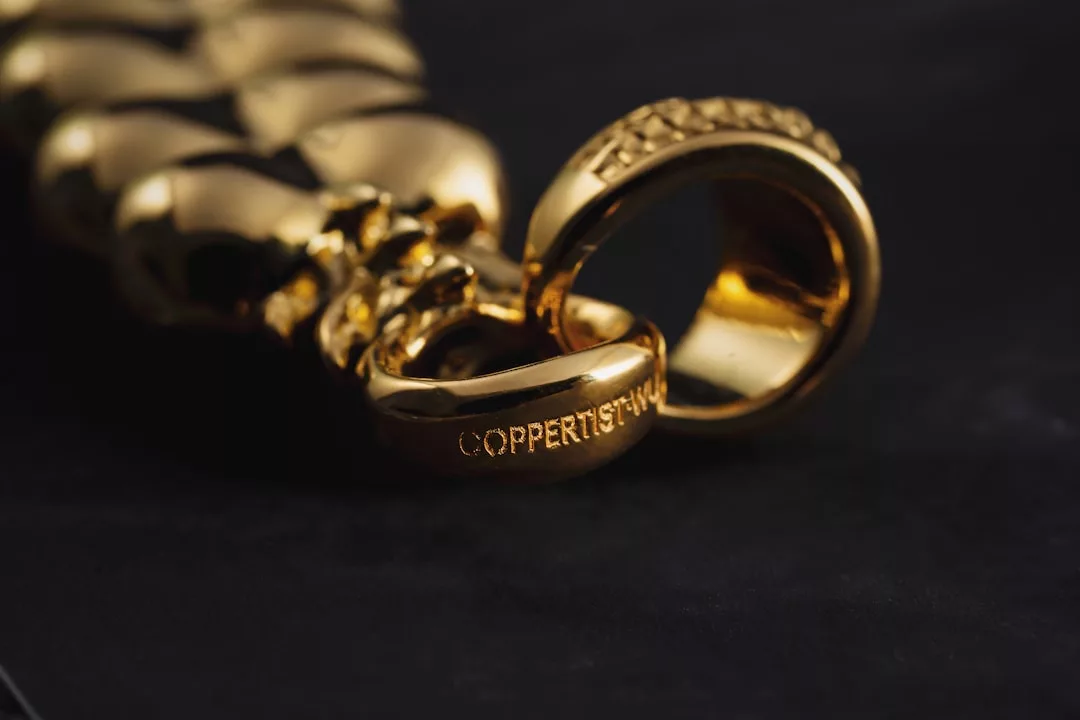 Close-up of a gold chain with a clasp on a dark surface; "COPPERTIST.WU" is engraved on the clasp, adding a touch of Glamesia fashion to your lifestyle.