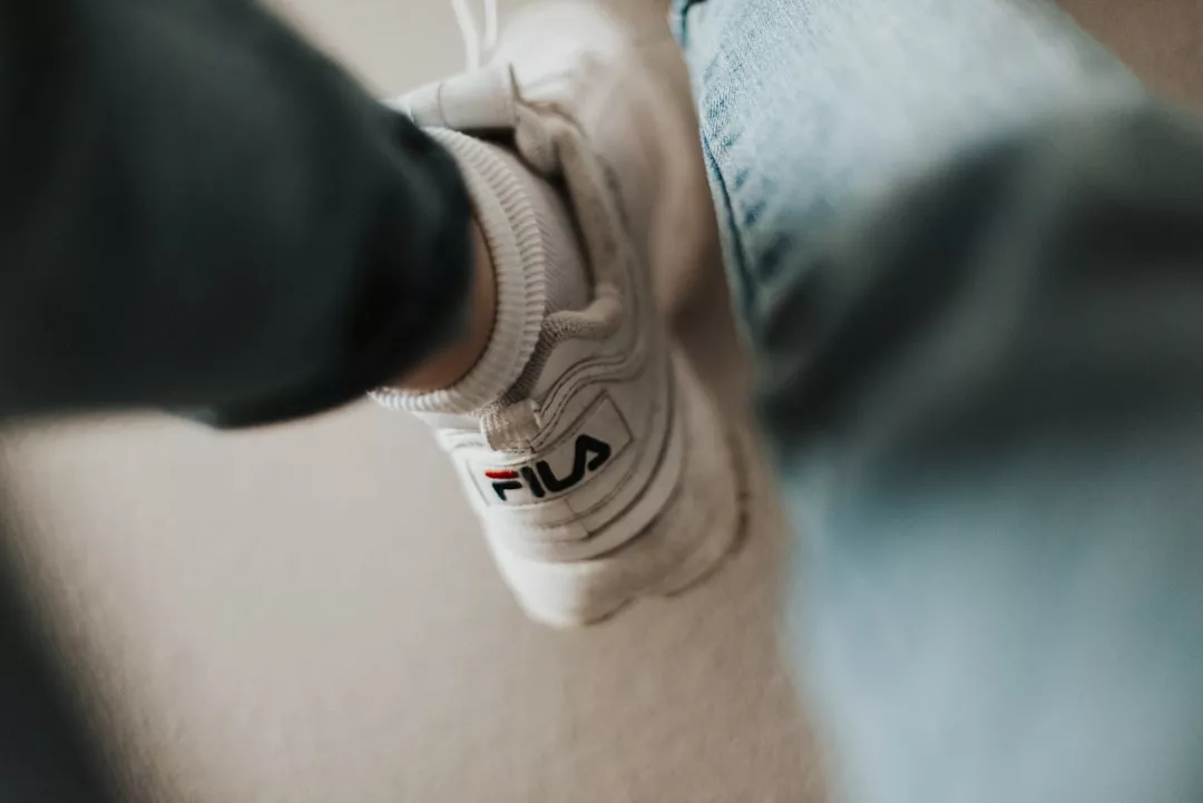 Close-up of a person wearing white Fila sneakers and denim jeans, with the Fila logo visible on the side—perfect for showcasing your everyday lifestyle.