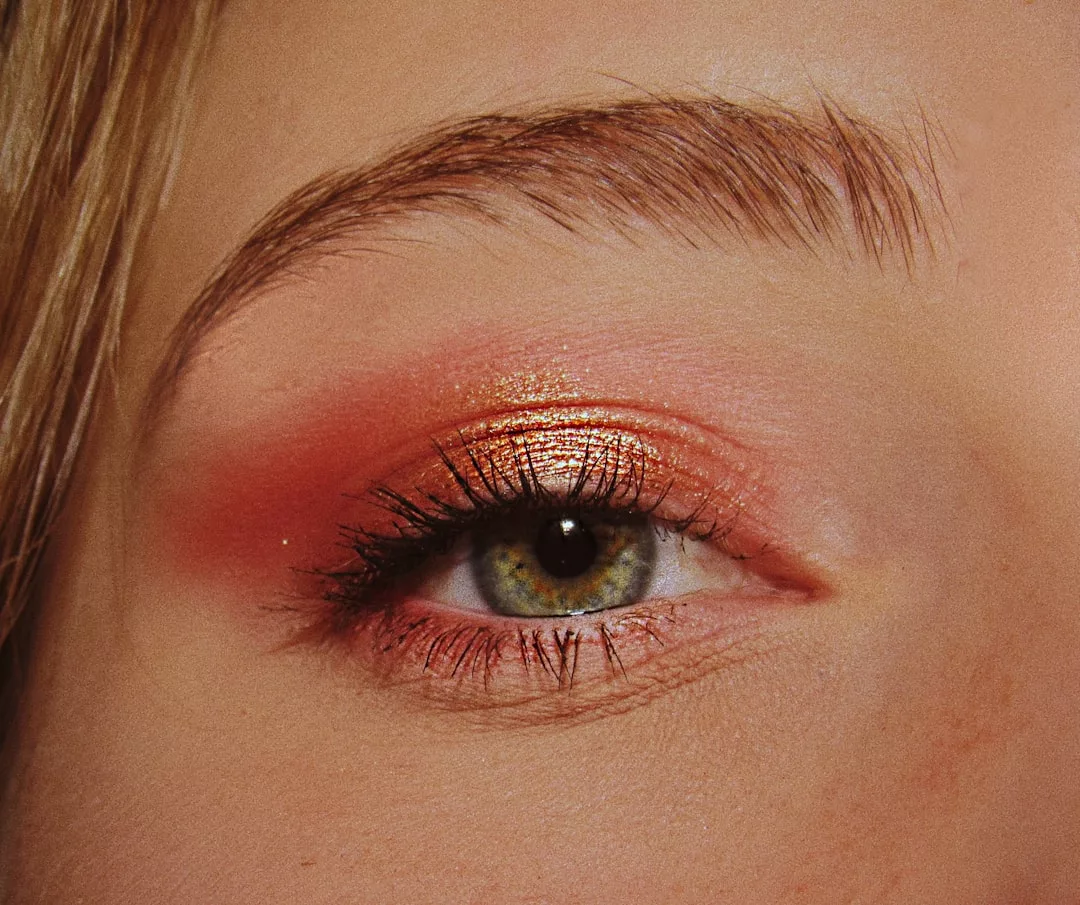 Close-up of a green eye with thick lashes and warm-toned, shimmery orange eyeshadow blended on the eyelid and crease—a Glamesia look perfect for modern fashion lovers.
