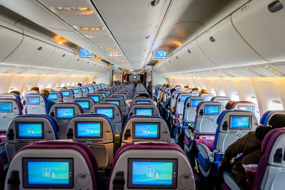 The image shows the interior of an airplane cabin with rows of economy class seats, each equipped with personal screens, offering a glimpse into the relaxed travel lifestyle enjoyed by Glamesia passengers seated sparsely throughout.