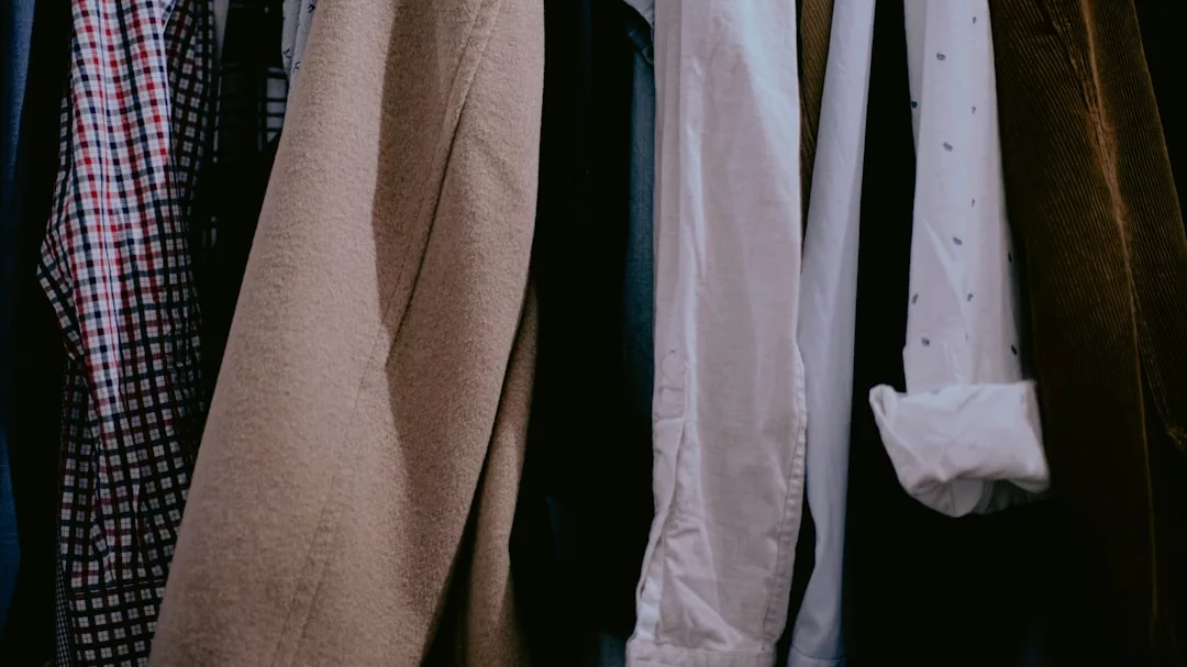 A close-up view of various shirts, jackets, and coats hanging on a rack, featuring luxury checkered, beige, white, and brown clothing items.