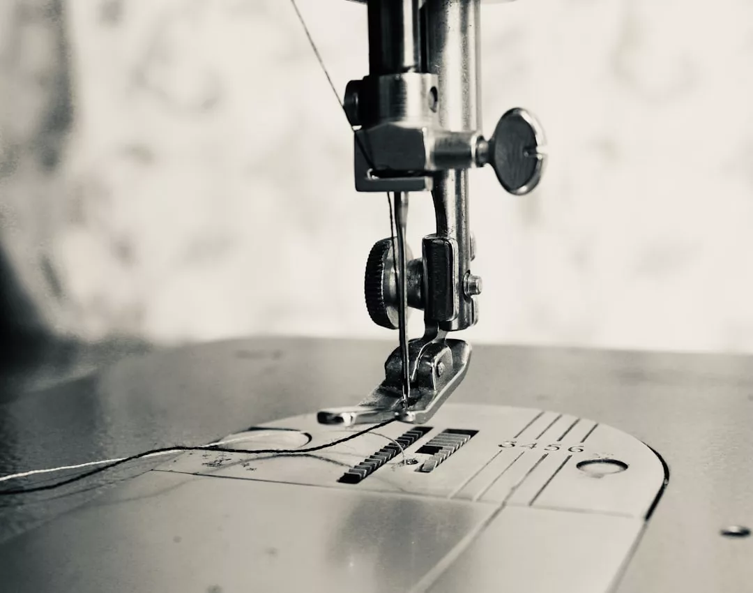 Close-up of a sewing machine needle and presser foot, with thread passing through the needle over the metal needle plate—a glimpse of Glamesia luxury and lifestyle in every detail.