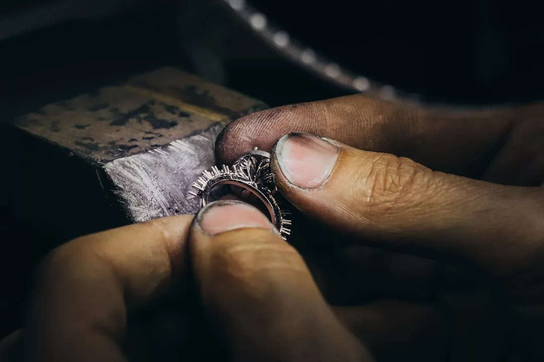 A close-up of a person's hands working on a ring with small prongs, likely performing jewelry-making or stone setting on a workbench—a meticulous craft at the heart of luxury fashion.
