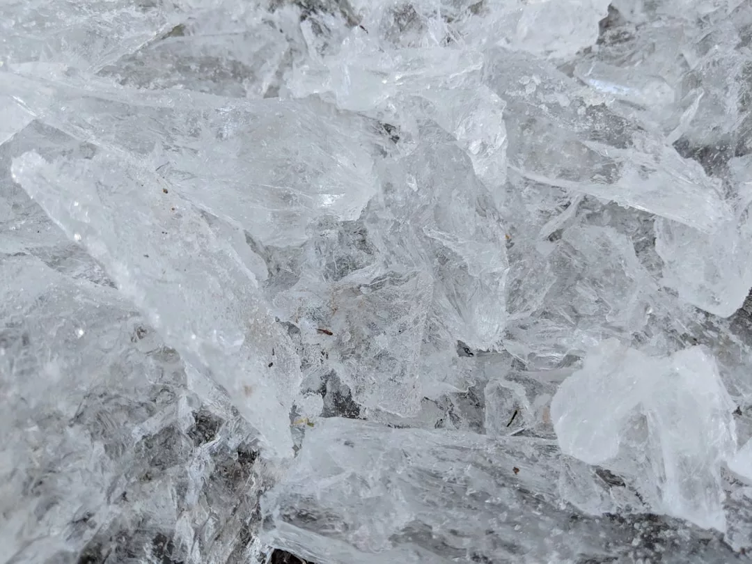 A close-up view of several overlapping clear ice chunks, with jagged edges and varying thicknesses, creating a textured surface that exudes an air of natural luxury.