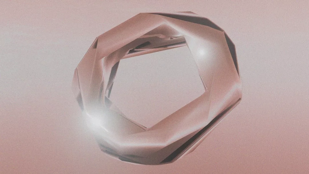 A faceted, metallic ring with a geometric, angular design floats against a pale pink background, reflecting light at a few points—a true Glamesia piece for modern lifestyle elegance.