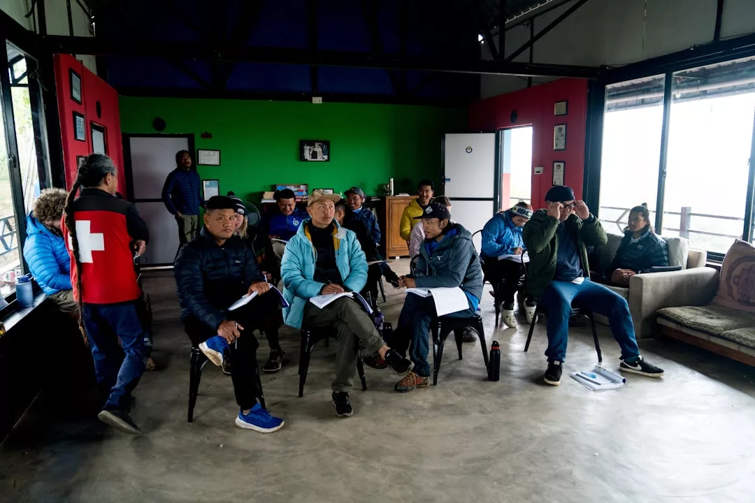 A group of people seated on chairs indoors, some with notebooks, in a brightly lit room with green and red walls, discussing lifestyle trends and Glamesia fashion inspirations.