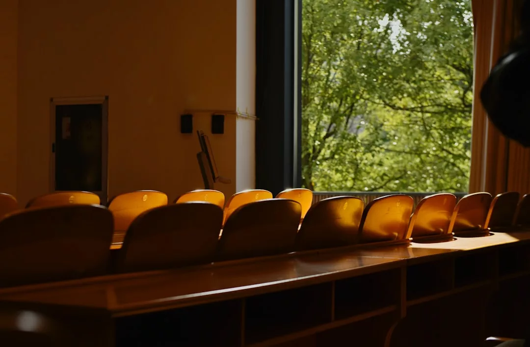 Rows of empty wooden chairs in a sunlit classroom or lecture hall, with a large window revealing green trees outside—a serene setting that reflects the calm luxury of the Glamesia lifestyle.