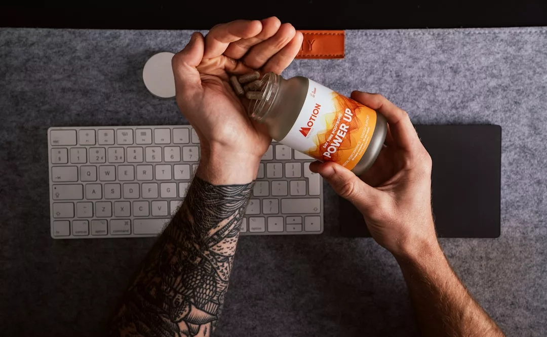 Person pouring supplements from a bottle labeled "Power Up" into their hand above a keyboard and mousepad on a luxury desk setup.